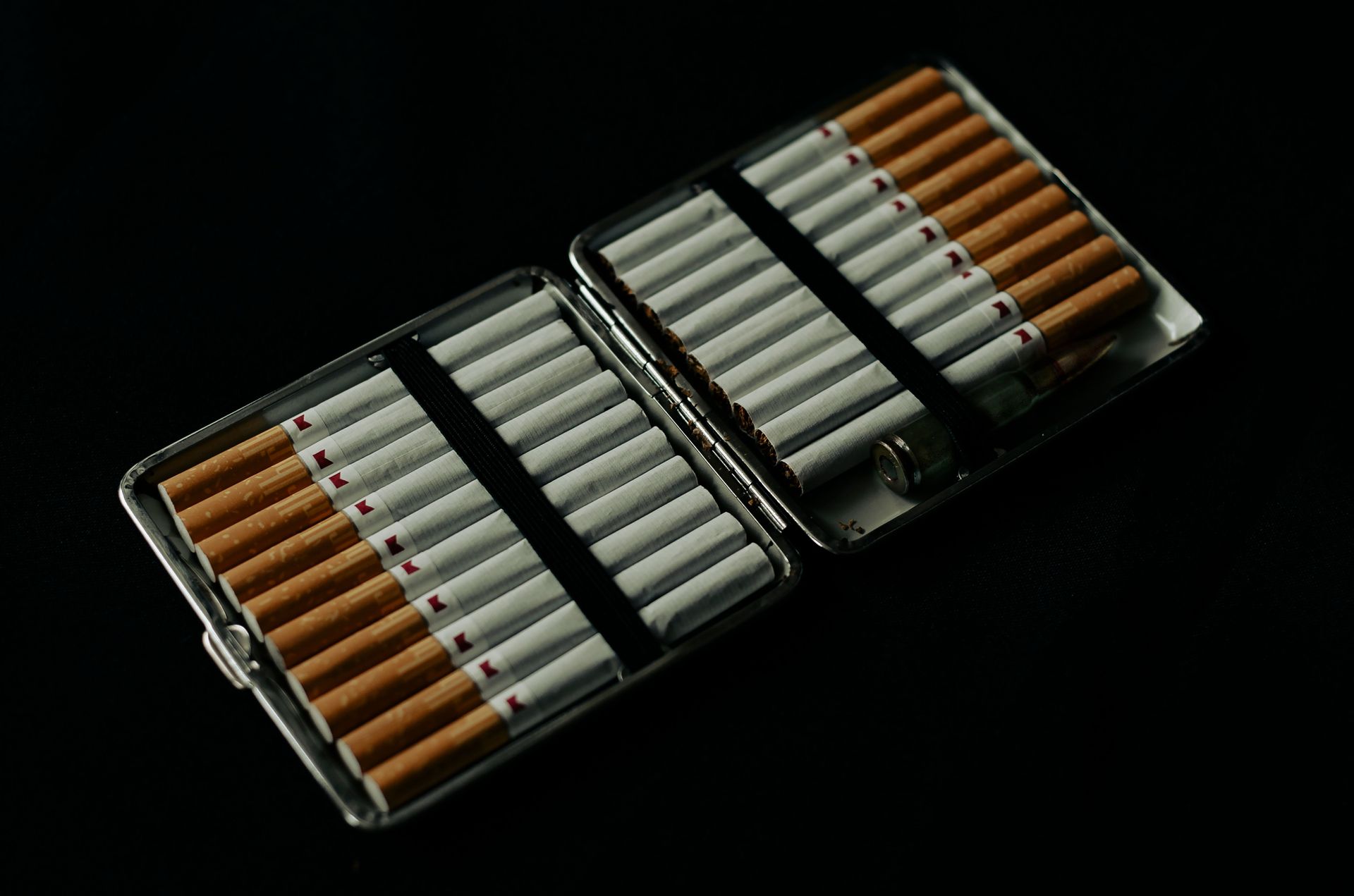 Cigarette case open with several cigarettes inside on a dark background, conveying a moody and dramatic tone.